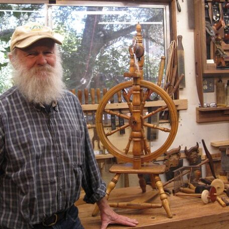 Tom Spittler in his wood working shop next to a castle spinning wheel.